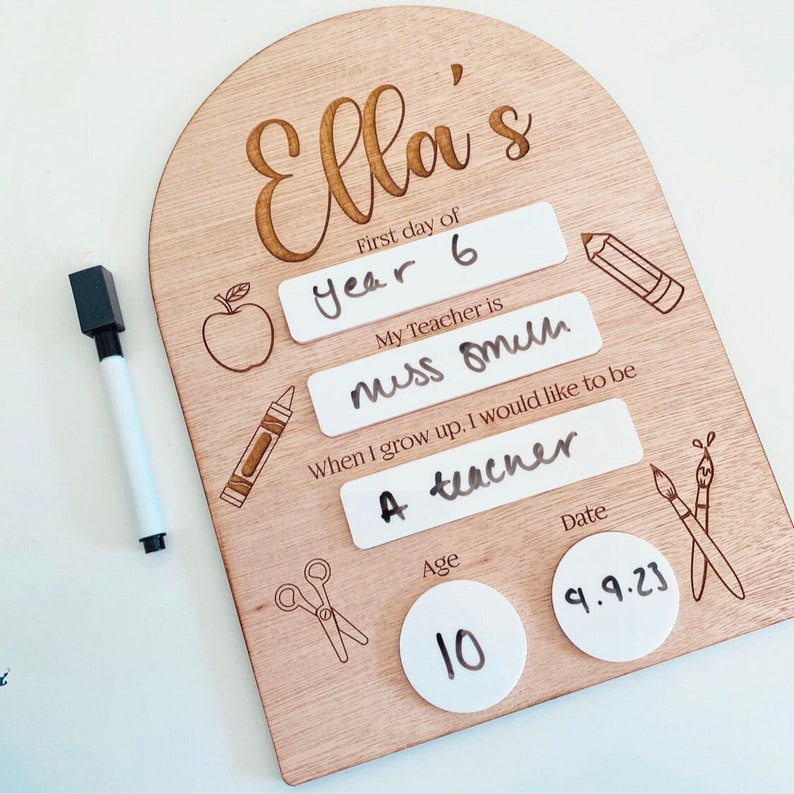 May include: A wooden sign with a personalized message for a student's first day of school. The sign includes the student's name, Ella, the grade they are entering, year 6, their teacher's name, miss omilh, their future career aspiration, a teacher, their age, 10, and the date, 9.9.23.