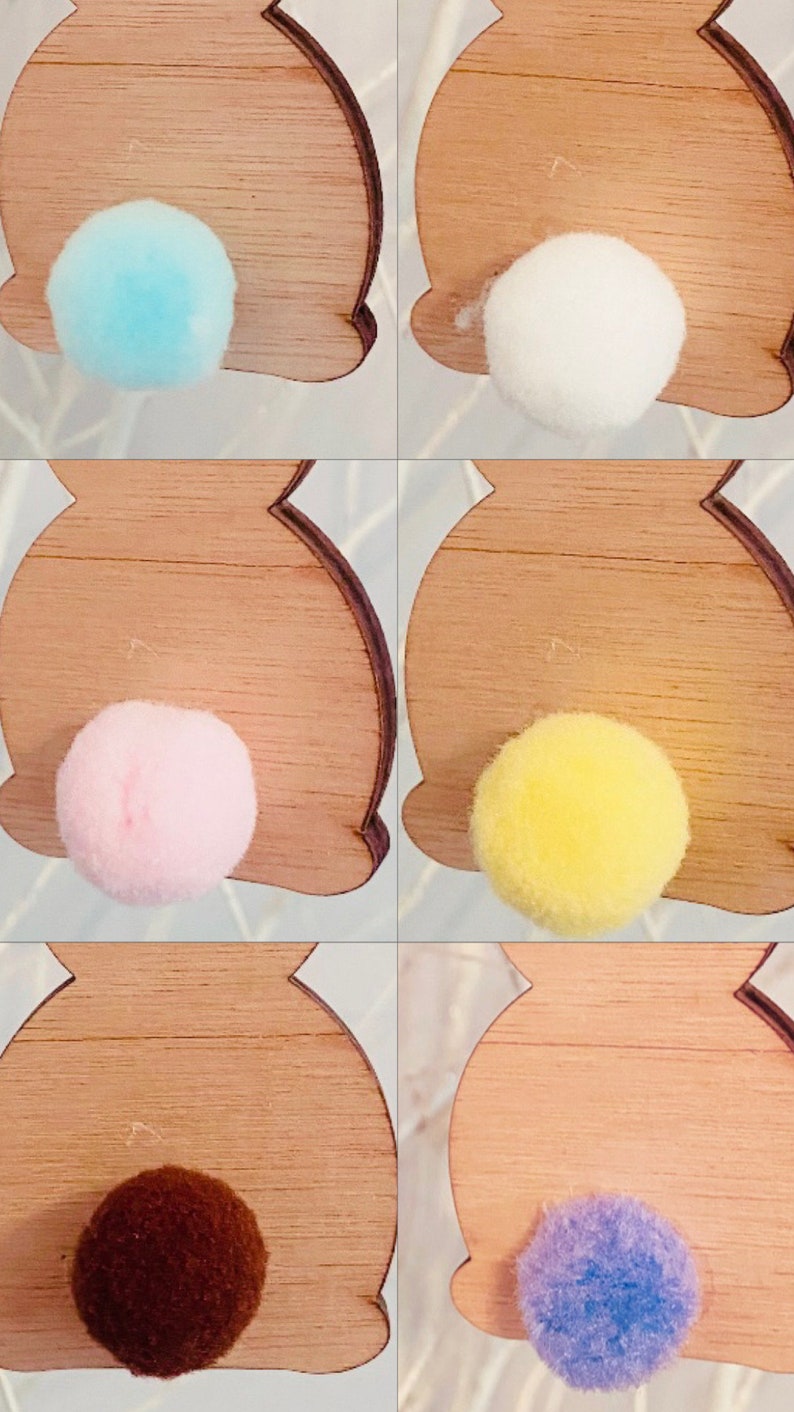 May include: Five wooden bunny shapes with different colored pom-poms attached to the back. The colors are light blue, white, pink, yellow, and brown.