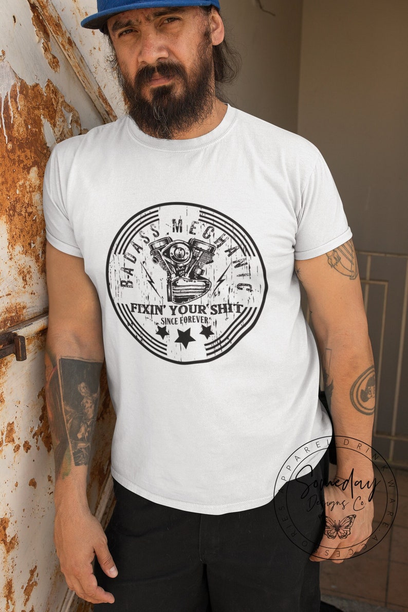 May include: White t-shirt with a black and white graphic of a motorcycle engine with the text "Badass Mechanic Fixin' Your Shit Since Forever."