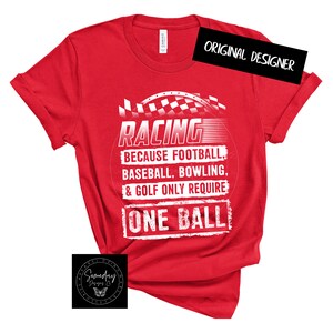 Op de afbeelding: Rood T-shirt met een witte afbeelding waarop staat "RACING BECAUSE FOOTBALL, BASEBALL, BOWLING, & GOLF ONLY REQUIRE ONE BALL". De afbeelding bevat ook een geruit vlagontwerp.