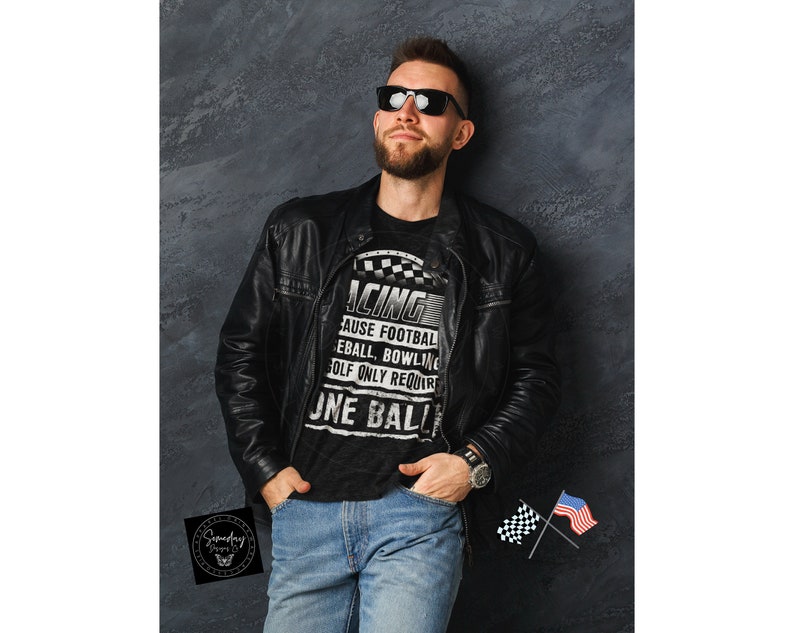 Op de afbeelding: Een man draagt een zwart T-shirt met een witte afbeelding waarop staat "Racing because football, baseball, bowling, golf only requires one ball". Hij draagt een zwart leren jack en een blauwe jeans. Hij staat voor een grijze muur.