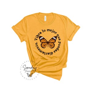K&ouml;nnte beinhalten: Gelbes T-Shirt mit einem schwarzen Kreis-Motiv mit einem Schmetterling und dem Text "Vibra lo mejor que puedas diariamente."