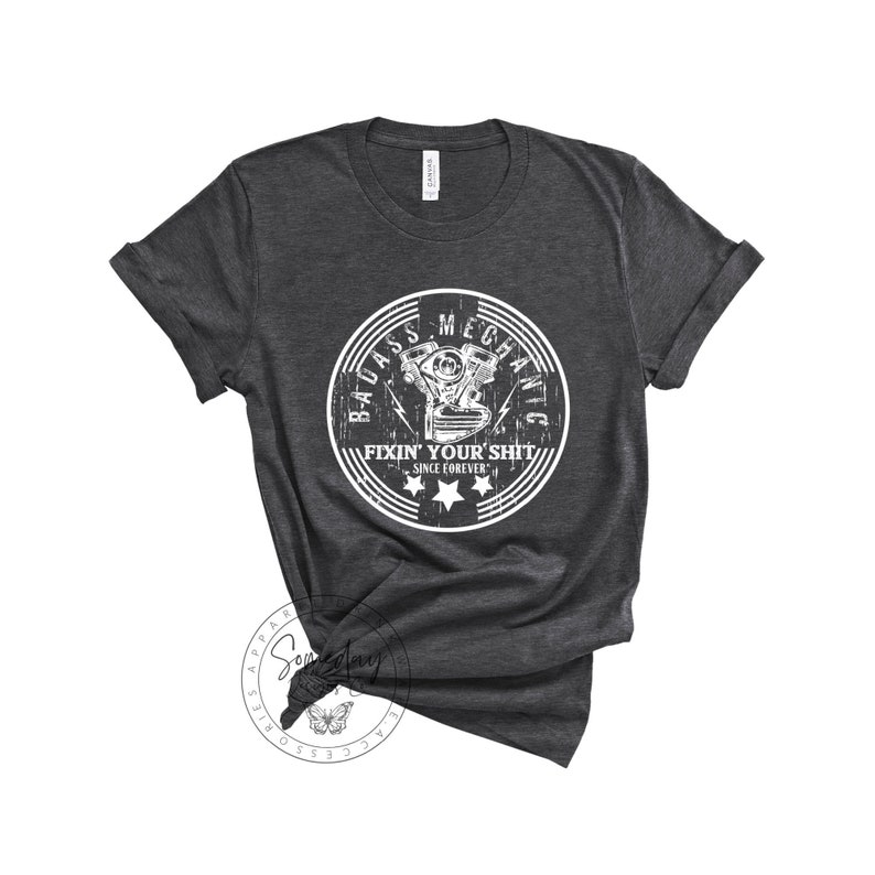 May include: A dark gray t-shirt with a white distressed circle graphic that says "Badass Mechanic Fixin' Your Shit Since Forever" with a stylized engine illustration inside the circle.