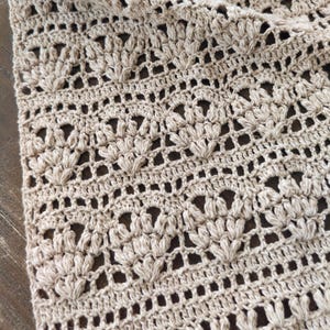 Puede incluir: Primer plano de una tela de crochet beige con un patrón repetitivo de pequeñas formas de flores.