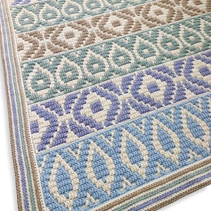 May include: A rectangular crochet blanket featuring horizontal bands of geometric and teardrop patterns in shades of light blue, periwinkle, sage green, and beige. The design is worked in a textured stitch with a cream-colored border trim.