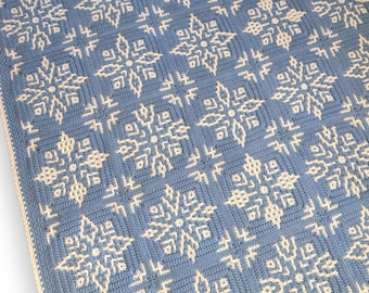 May include: A handmade, crocheted blanket with a repeating snowflake design. The blanket is mainly light blue with off-white snowflakes. The edges have a cream-coloured border. The design is intricate and detailed, suitable for winter decor.