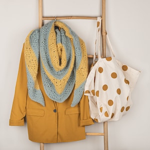 May include: A yellow blazer with a blue and yellow crocheted scarf hanging on a wooden ladder with a white tote bag with brown polka dots.