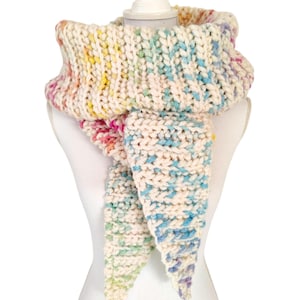 Könnte beinhalten: Ein weißer Häkel-Schal mit einem Regenbogen-Ombre-Muster. Der Schal ist gefaltet und auf einer weißen Schaufensterpuppe ausgestellt.