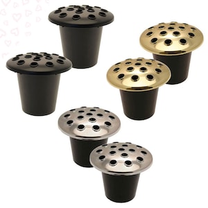 May include: Five black plastic flower pots with different coloured metal tops. The tops have multiple holes for flower stems. The pots are for use at a cemetery or memorial.