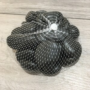 May include: A bag of black polished river rocks in a white mesh bag. The bag is tied with a white twist tie.