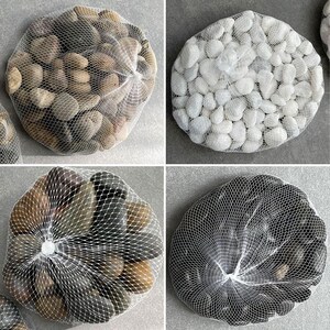 May include: Four separate mesh bags containing smooth, rounded stones in distinct colour variations. One bag holds tan and brown stones, another contains white stones, a third features mixed dark grey and brown stones, and the fourth holds black stones.