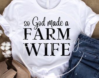 Puede incluir: Camiseta blanca con texto negro que dice "So God made a FARM WIFE". La camiseta está colocada sobre una superficie de arpillera marrón con un par de pantalones vaqueros azules y botas marrones.