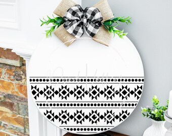 Puede incluir: Un letrero redondo de madera blanco con un patrón geométrico en blanco y negro. El letrero está decorado con un lazo de arpillera con una cinta a cuadros en blanco y negro.
