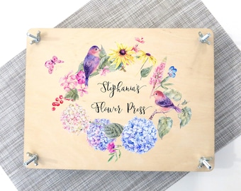 May include: A wooden flower press with a floral design and two birds. The text "Stephania's Flower Press" is printed on the front.