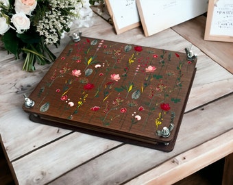 May include: A brown wooden photo album with a floral design featuring pink, red, and yellow flowers. The album has metal clasps and is closed.