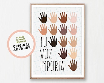 May include: A framed art print featuring a design of various skin-toned handprints. The Spanish text "TU VOZ IMPORTA" is displayed below the handprints. The artwork is displayed above a gray sofa with decorative pillows and a green throw blanket.