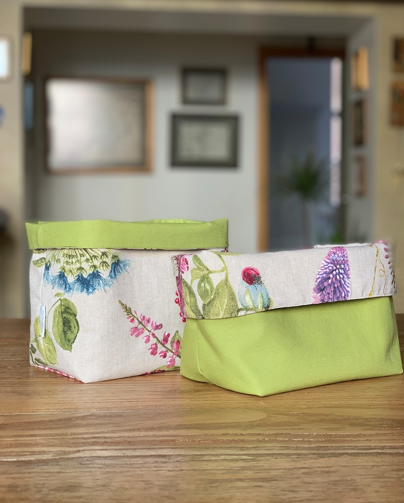 May include: Two green and white fabric storage baskets with floral patterns. The larger basket has a green top and the smaller basket has a green bottom.