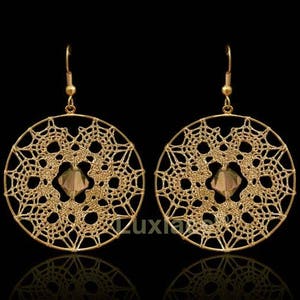 May include: Gold tone earrings with a delicate, circular, lace-like design and a small, clear crystal in the centre.