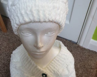 May include: White knitted hat and matching cowl with teal buttons. The hat and cowl are made with a fluffy yarn.