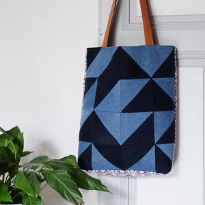Peut inclure: Un sac cabas géométrique bleu et noir avec des anses en cuir marron. Le sac est en jean et a un design patchwork.