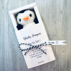 May include: A white gift box with a black and white penguin plush toy inside. The box has a white tag with the text "Gl&uuml;cks-Pinguin Nur f&uuml;r Dich!" and a white tag with the text "F&uuml;r Dich" with a heart symbol.