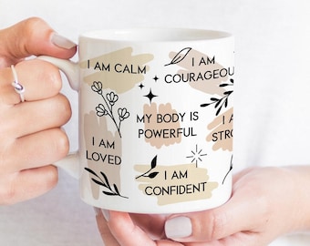 May include: White ceramic mug with black text and illustrations. The text reads "I am calm", "I am loved", "I am courageous", "My body is powerful", "I am confident", and "I am strong".