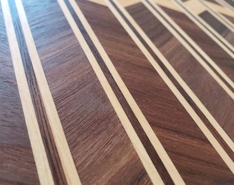 Op de afbeelding: Een close-up van een houten snijplank met een visgraatpatroon. De plank is gemaakt van walnoot- en esdoornhout en heeft een natuurlijke afwerking.
