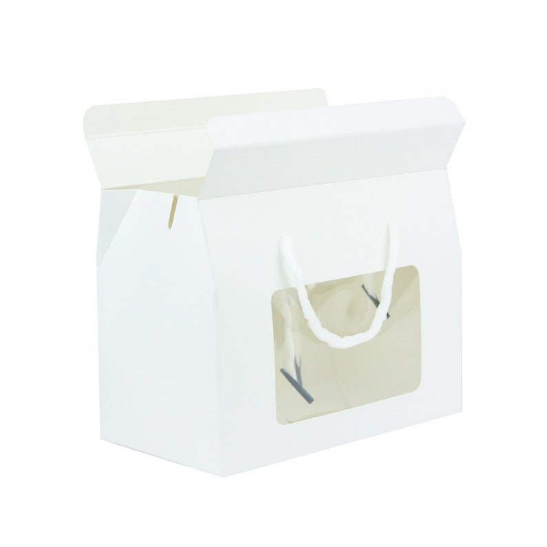 May include: White cardboard box with a clear window and a white rope handle. The box is designed for packaging and displaying baked goods.