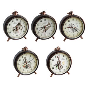 Può includere: Cinque sveglie nere e bronzo con quadranti color crema. Ogni quadrante presenta un diverso strumento musicale: pianoforte, tromba, macchina da scrivere, grammofono e violino. Gli orologi hanno un'estetica classica e vintage.