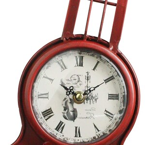 May include: Red metal clock shaped like a guitar with Roman numeral markings on the face. The clock face has a white background with black Roman numerals and a black and gold hour and minute hand. The clock face also has a small black and white image of a violin and the text "Premiere" and "Geneva".