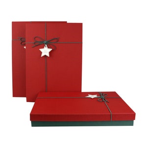 May include: Three red gift boxes with green detailing. Each box is tied with green string and a star-shaped tag. The boxes are rectangular and have a textured surface. The bottom box is a square shape.