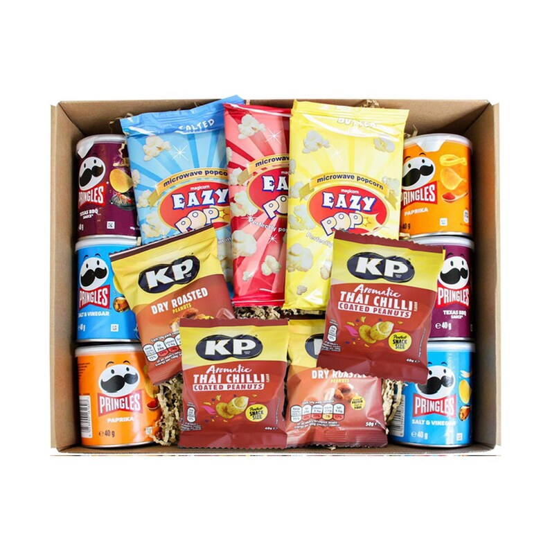May include: A brown cardboard box filled with various snack foods, including bags of microwave popcorn, peanuts, and cans of Pringles. The box is filled with shredded paper and the snacks are arranged in a visually appealing way.