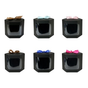 Puede incluir: Seis cajas de regalo hexagonales negras con ventanas transparentes y lazos de cinta de diferentes colores. Las cajas están dispuestas en dos filas de tres. Los lazos son marrones, azul claro, rosa, marrones, azules y rosas.