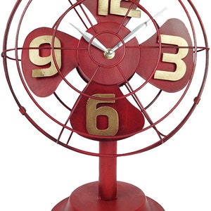 May include: Red metal tabletop clock shaped like a vintage fan with gold numbers. The clock has a white face and black hands.