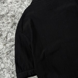 May include: A solid black blazer featuring a textured fabric with vertical ribbed detailing, a notched lapel collar, and three-quarter length sleeves with cuffed hems. The garment is constructed with a structured shoulder design and a clean finish.