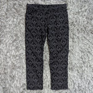 May include: A pair of pants featuring a dark black and charcoal gray damask pattern. The garment has a straight-leg cut with a standard waistband and a repeating ornate scrollwork design that covers the entire surface of the fabric.