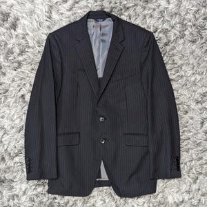 May include: A dark gray pinstripe blazer with a two-button closure. The blazer has a notched lapel, a chest pocket, and two front pockets. The sleeves have four buttons. The interior lining is a light gray color.