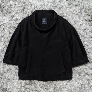 May include: A black jacket with a high collar, three-quarter length sleeves, and two vertical front pockets. The garment features a textured fabric surface and a dark interior label with the white text LIMI feu visible at the neckline.