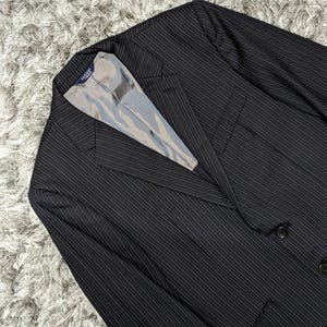 May include: A black pinstripe blazer with a light gray lining. The blazer has a classic two-button closure and a notched lapel. The fabric has a subtle vertical stripe pattern.