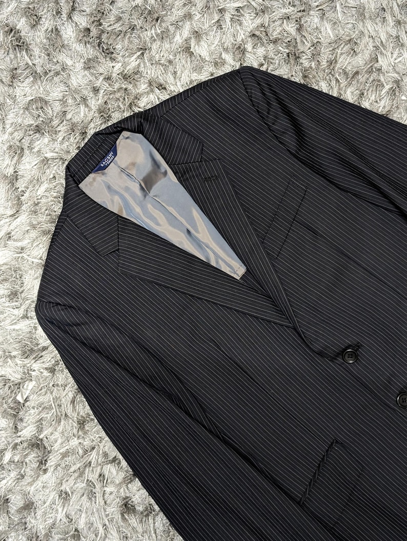 May include: A black pinstripe blazer with a light gray lining. The blazer has a classic two-button closure and a notched lapel. The fabric has a subtle vertical stripe pattern.