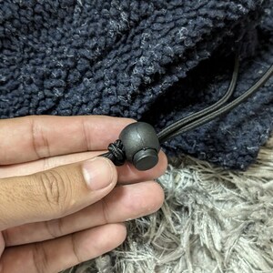 May include: Close-up of a navy blue fleece fabric with a drawstring and a black cord lock. The fabric has a textured, fuzzy appearance. The cord lock is round and made of black plastic.