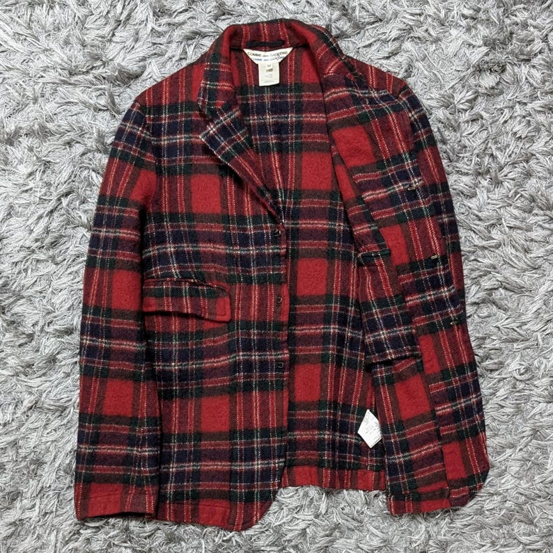 May include: A red and black plaid blazer with a two-button closure and two front pockets. The jacket has a classic lapel collar and is made of a textured fabric. The blazer is a medium weight and suitable for cooler weather.