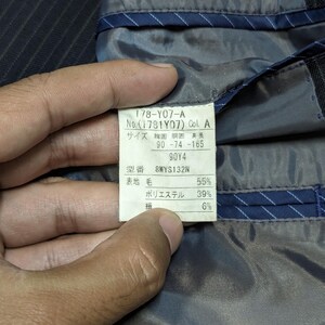 May include: Close-up of a label inside a dark pinstripe suit jacket. The label displays text in Japanese, including size and material composition percentages: 55% wool, 39% polyester, and 6% other.