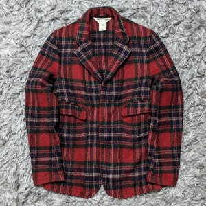 May include: A red, black, and navy plaid blazer with a notched collar and two front pockets. The jacket has a classic fit and is made of a textured fabric. The blazer is a stylish outerwear option.