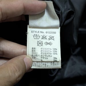 Peut inclure: Gros plan sur une &eacute;tiquette de v&ecirc;tement avec le texte "STYLE No. 6122050". L'&eacute;tiquette indique la composition du tissu : 100% polyester pour les couches ext&eacute;rieure et int&eacute;rieure, 70% acrylique et 30% laine pour les bord-c&ocirc;tes. Instructions de lavage incluses.