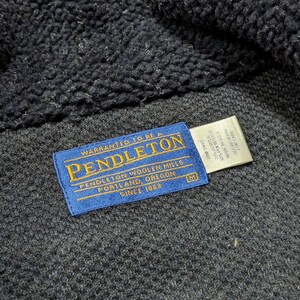 May include: Close-up of a dark navy blue Pendleton jacket. The blue label reads "PENDLETON WOOLEN MILLS PORTLAND, OREGON SINCE 1863". The jacket has a textured, fuzzy interior and a woven exterior. A white tag with care instructions is also visible.