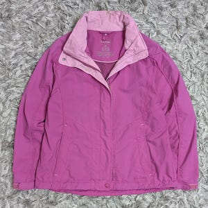 Può includere: Una giacca magenta L.L.Bean con colletto interno e fodera rosa più chiaro. La giacca presenta una chiusura frontale con zip, un'abbottonatura a pressione, maniche lunghe con polsini regolabili e due tasche laterali. Il logo L.L.Bean è visibile sul petto.