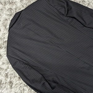 May include: Black pinstripe blazer. The blazer has a notched lapel and a two-button closure. The fabric has a subtle sheen, and the pinstripes are thin and white.
