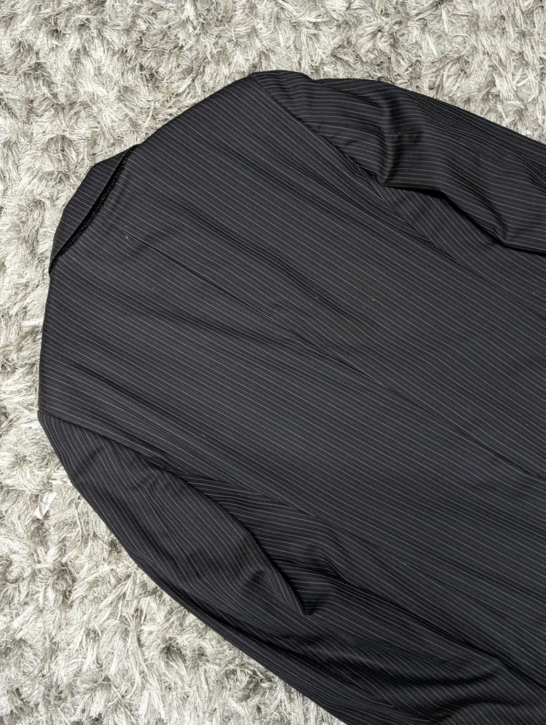 May include: Black pinstripe blazer. The blazer has a notched lapel and a two-button closure. The fabric has a subtle sheen, and the pinstripes are thin and white.