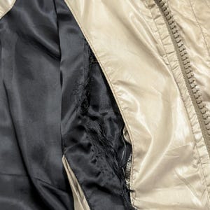 Peut inclure: Gros plan sur une veste beige avec une doublure noire. La veste est dot&eacute;e d'une fermeture &eacute;clair et d'un bouton. La doublure est d&eacute;chir&eacute;e, r&eacute;v&eacute;lant la construction int&eacute;rieure.